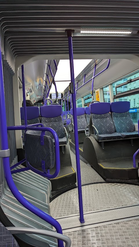 The interior of a Belfast Glider bus. There are purple and grey seats raised over the wheel arches, bright LED light panels on the ceiling, and a passenger information screen.