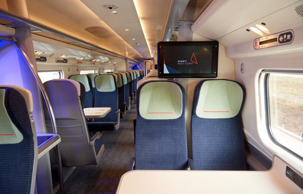 Image shows the refurbished interior of of a Pendolino train. The seats are navy blue and mint green, with an orange stripe on the headrest.